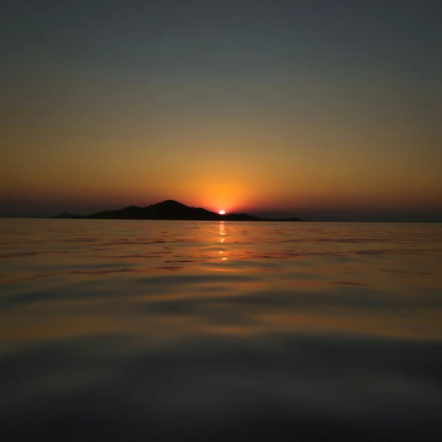 the sun sets behind a small island on a calm body of water