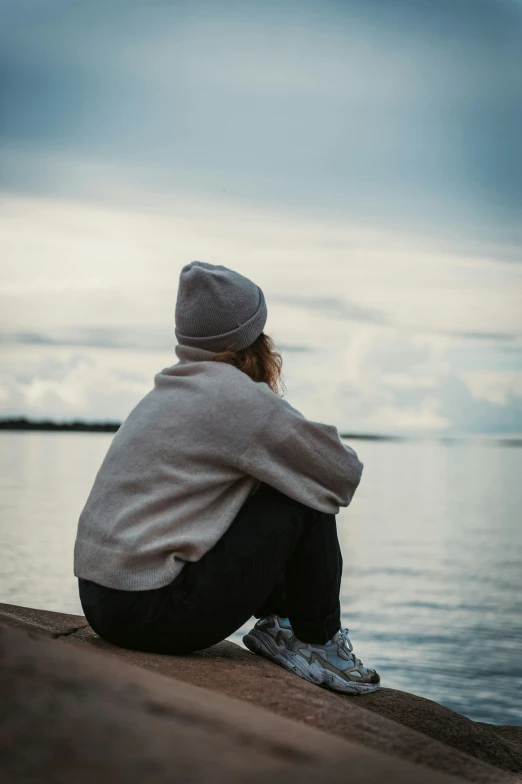 the woman sits near the water as she looks off into the distance