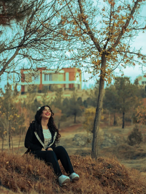 a young lady sitting under a tree in the autumn