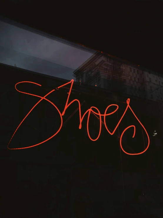 neon sign saying shoes and the city building behind