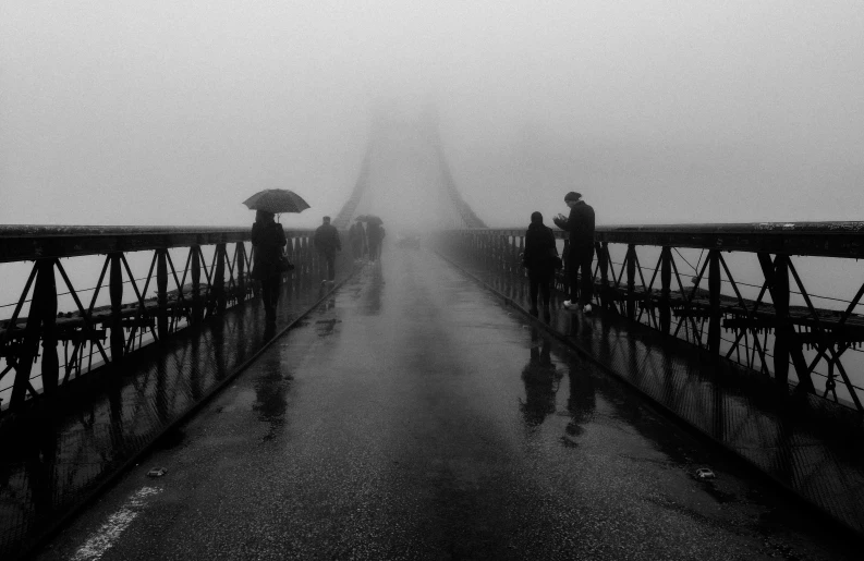 three people with umbrellas walk across a bridge on a gloomy day