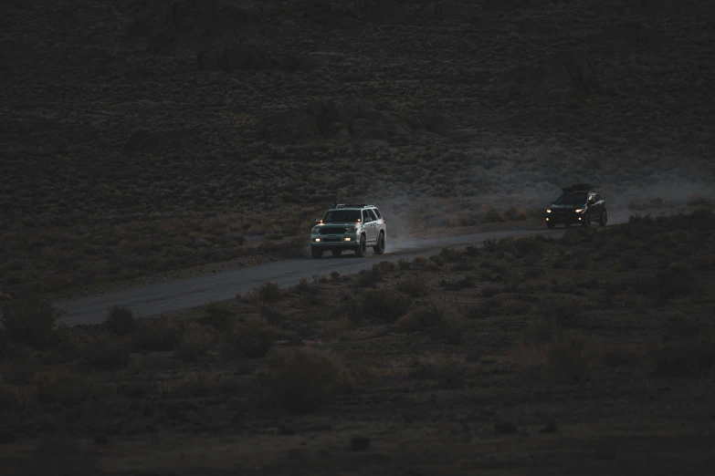 two trucks drive up a narrow dirt path in the middle of a dry grass field