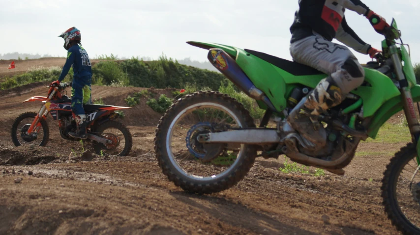 one person riding on a dirt bike and another standing up behind the motorcycle