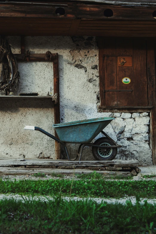 the wheelbarrow is leaning against the wall with a piece of machinery near it