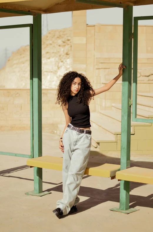 a woman in a black shirt and jeans standing by a wooden bench