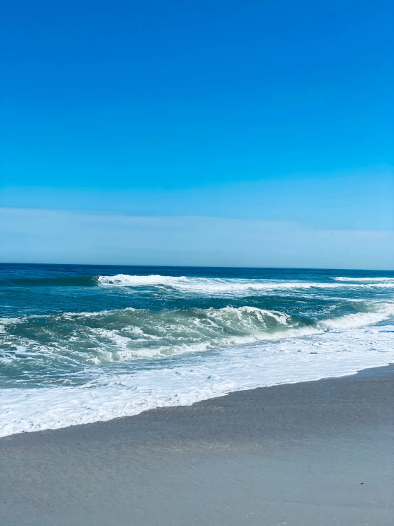 a surf boarder stands on the shore as a wave rolls in