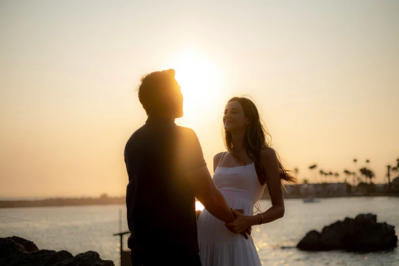 a bride and groom standing on the shore while the sun sets