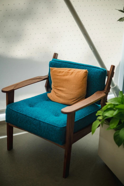 a chair sitting in front of a window with an orange pillow