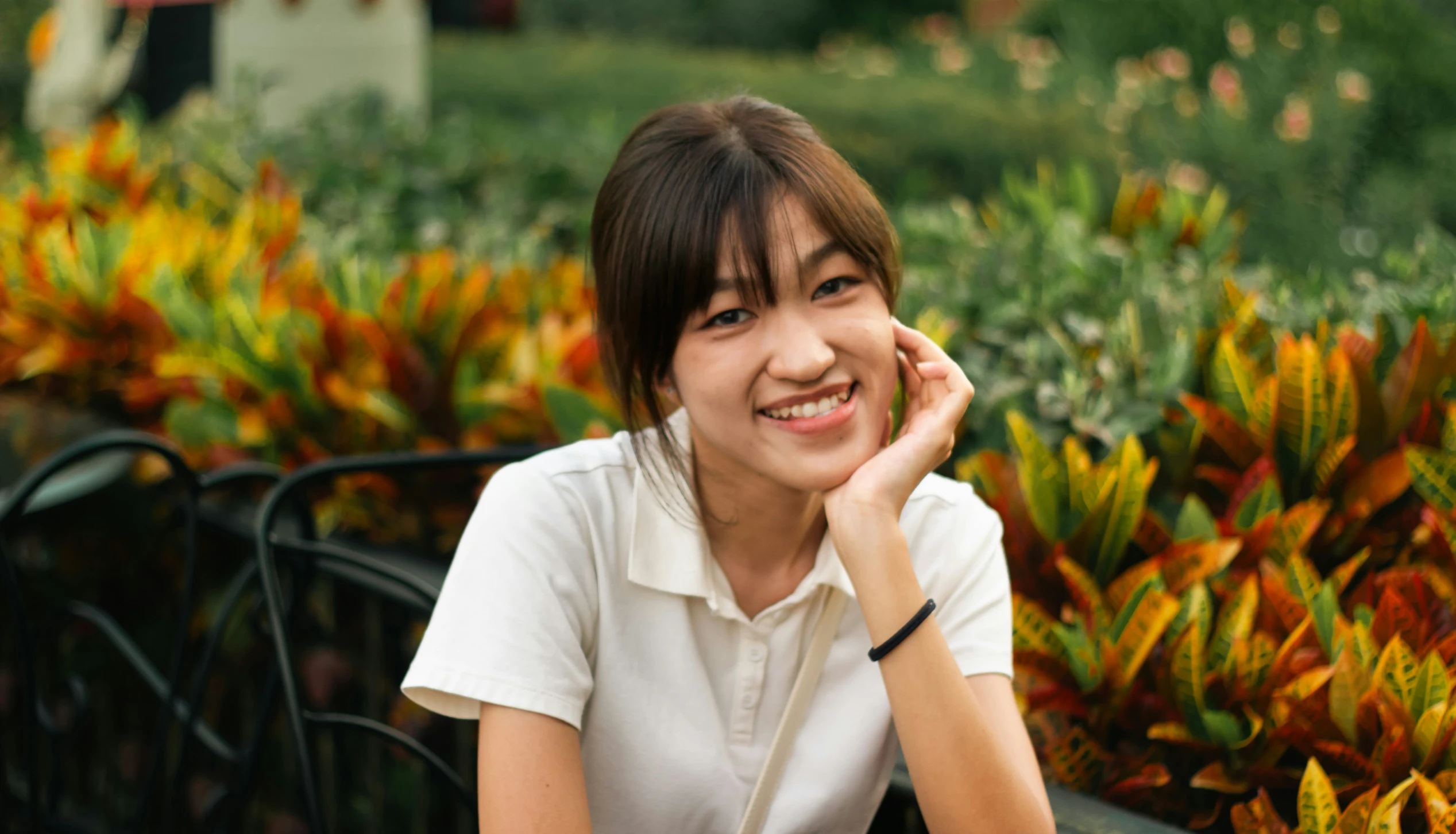 a beautiful young woman sitting outside in front of colorful bushes