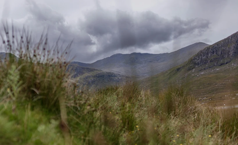 looking at some mountains from the top of a grassy hill