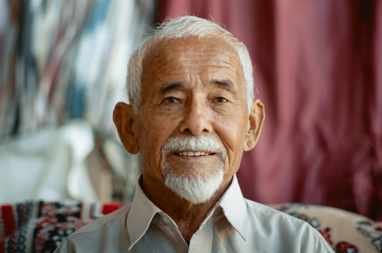 an old man smiles into the camera, wearing a shirt and tie