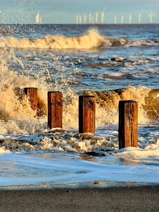 waves hitting on beach and wooden posts next to ocean