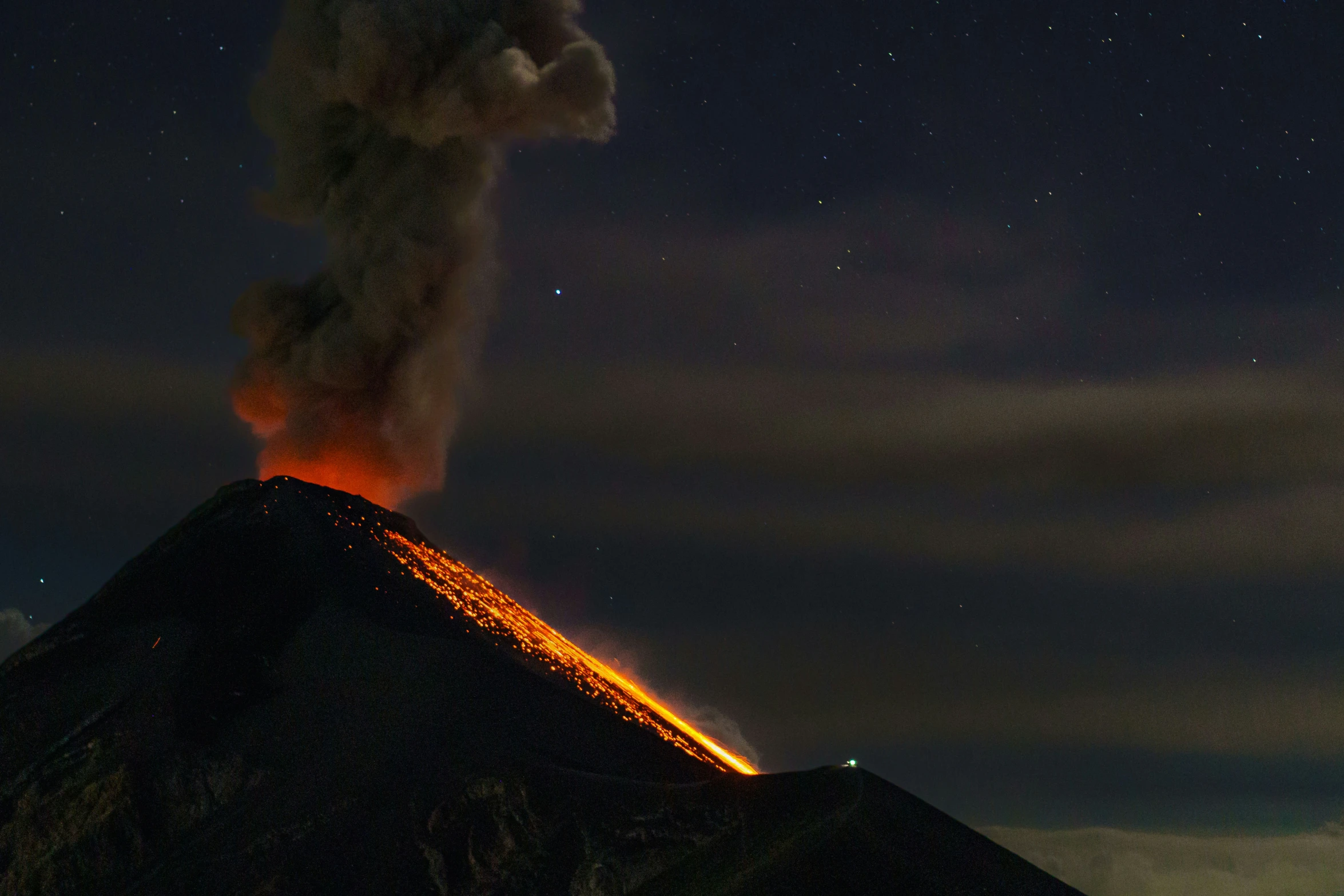 a mountain in the dark with a plume of smoke billowing out from top