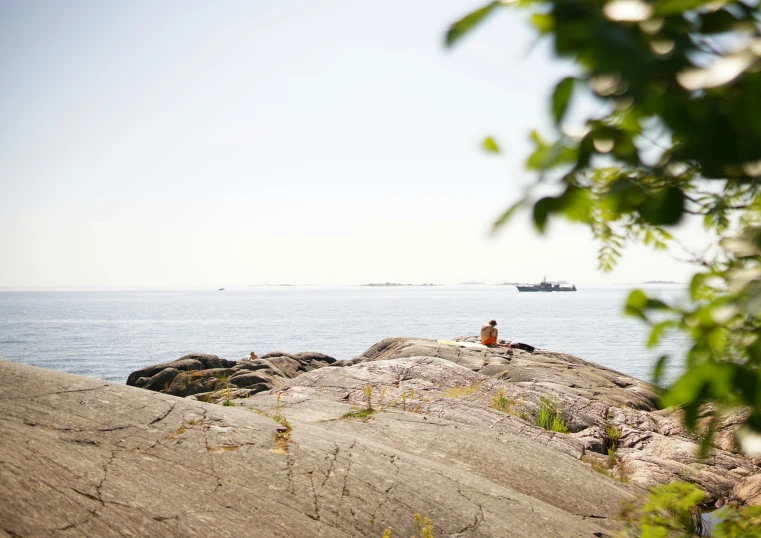 people sitting on a rock near the ocean watching a boat in the distance