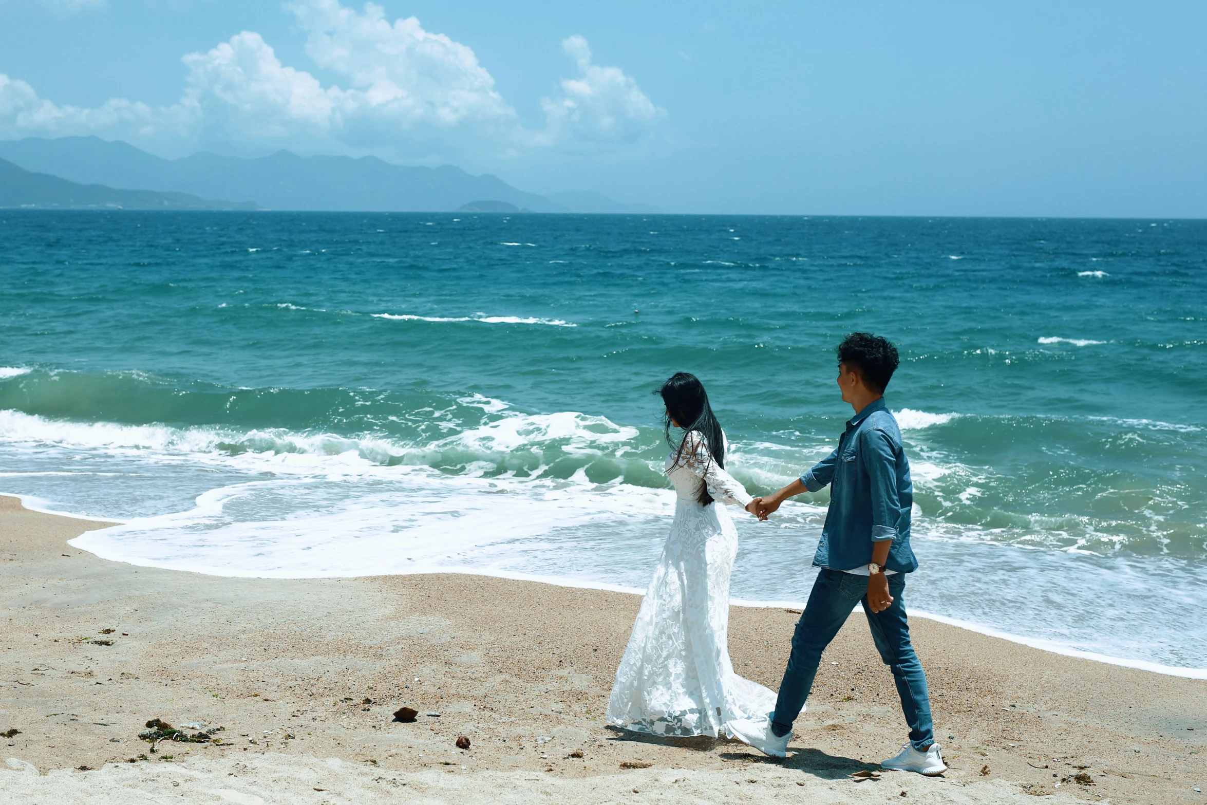 a bride and groom hold hands on the beach