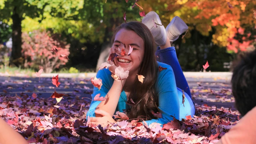 a smiling girl laying in some leaves and falling