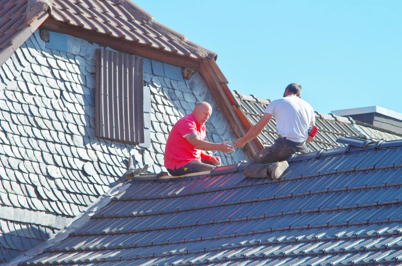 two men on top of a roof fixing a shingled roof