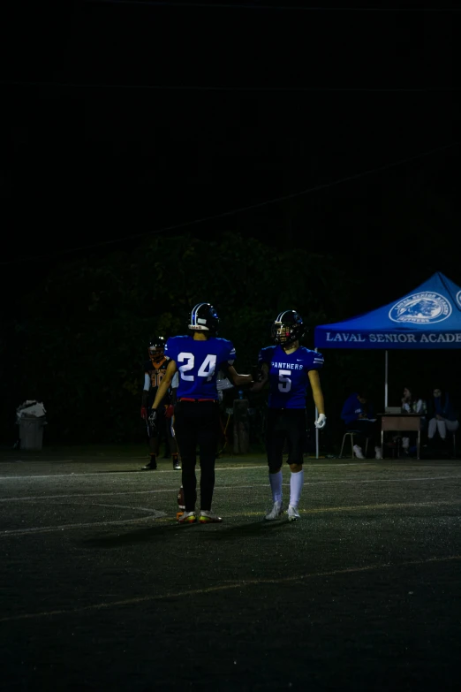 two high school football players holding hands at night