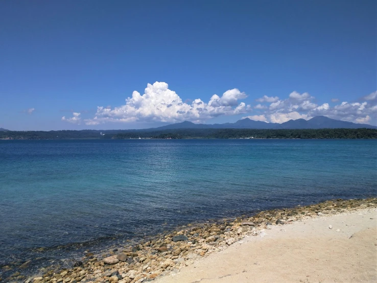 a sandy shore sits in the water as clouds loom above