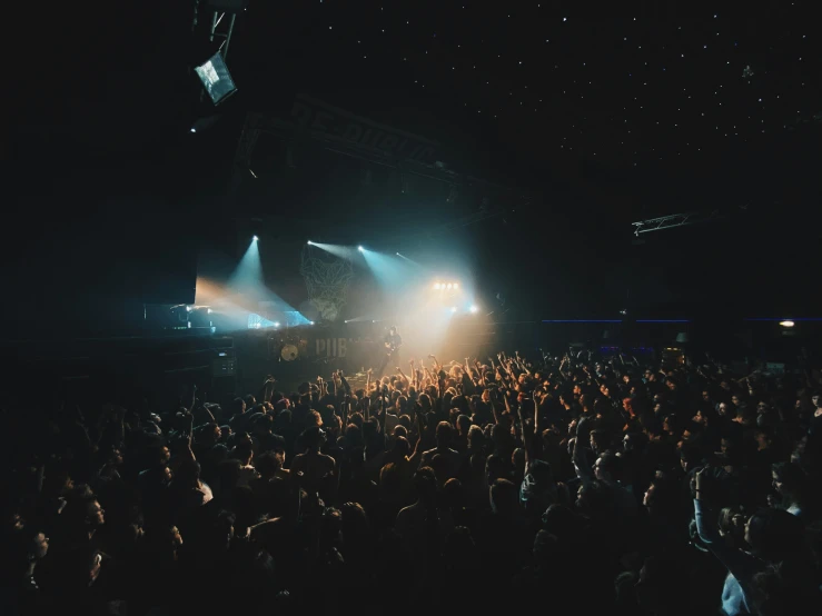 large crowd watching a concert on a dimly lit stage