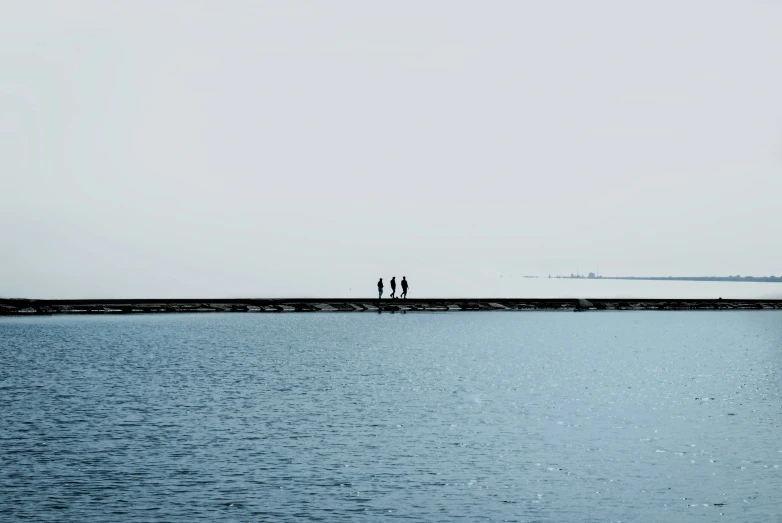 two people stand in front of the water looking out towards a pier