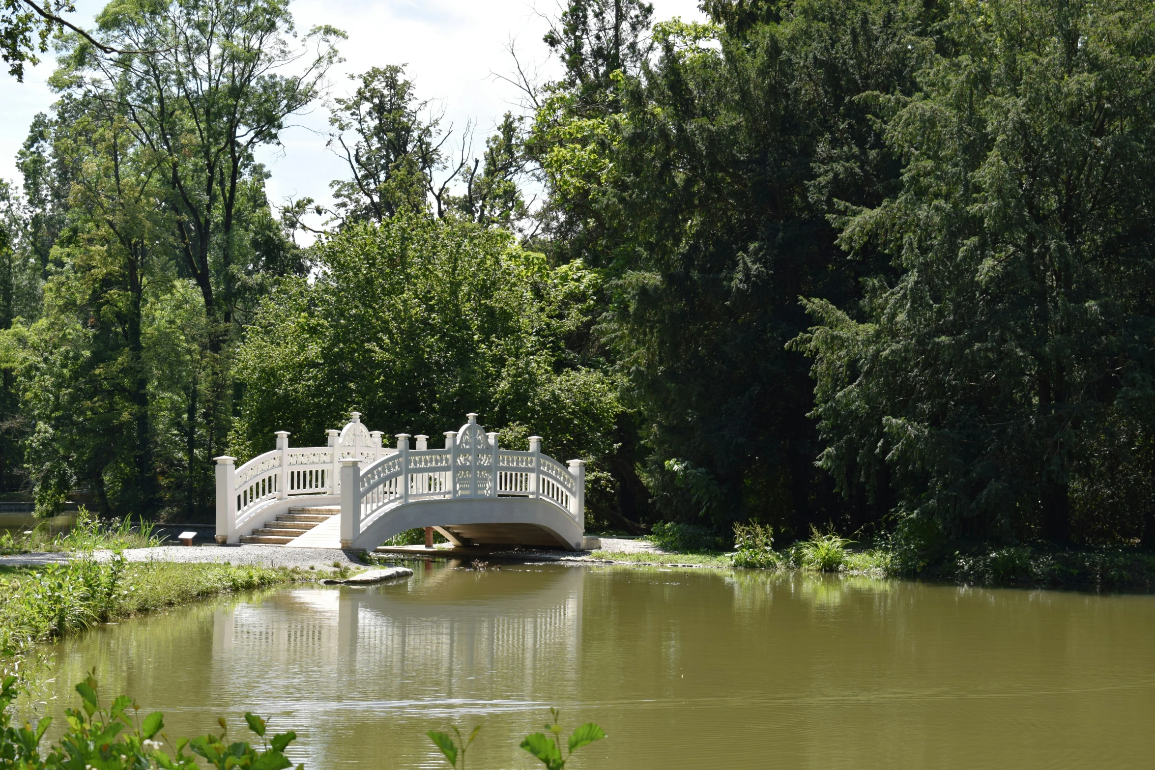 a bridge with steps crossing across a pond surrounded by trees