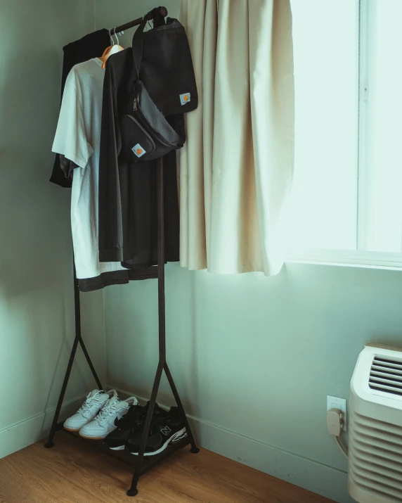 clothes are hanging in a black stand near the window