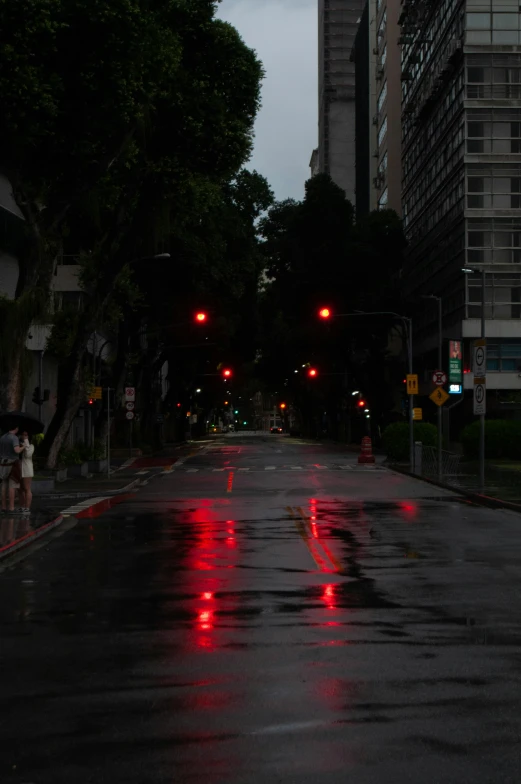 several red lights shine on the street as it rains