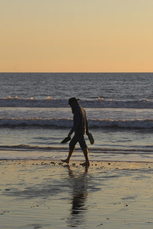 man walking on beach with surf board near ocean