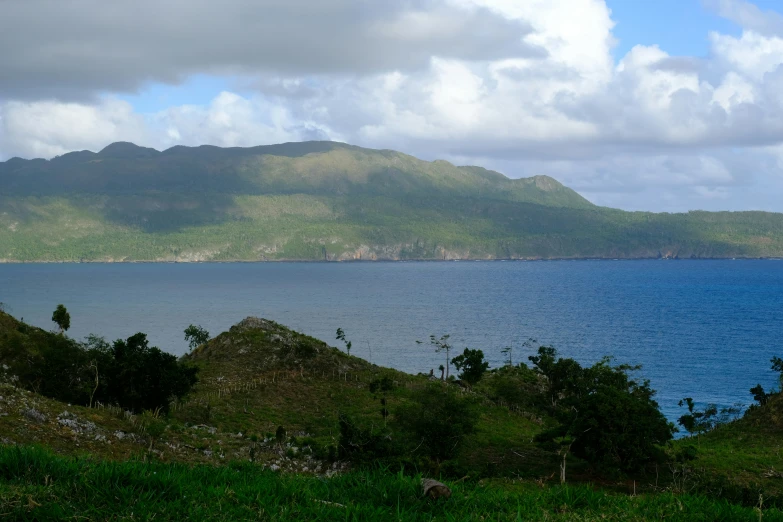 a lush green hill by the ocean under a cloudy sky