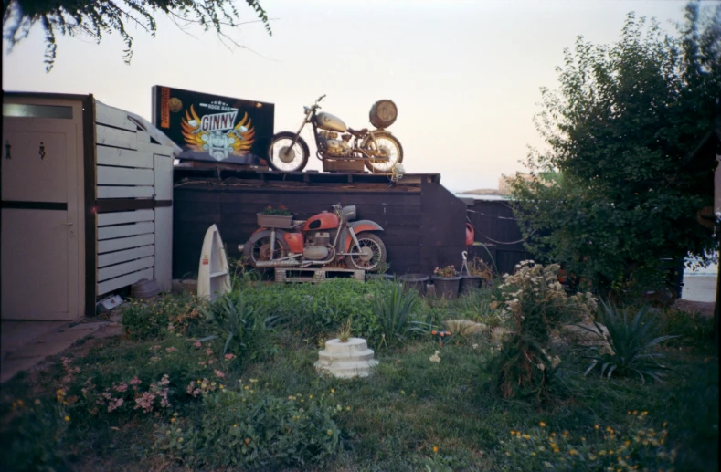 a motorcycle, a bicycle and other junk sit on top of the roof of a house