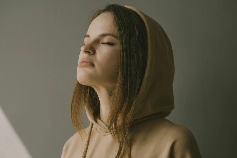 a woman with eyes closed and her hair ided, in a hooded sweatshirt and hood