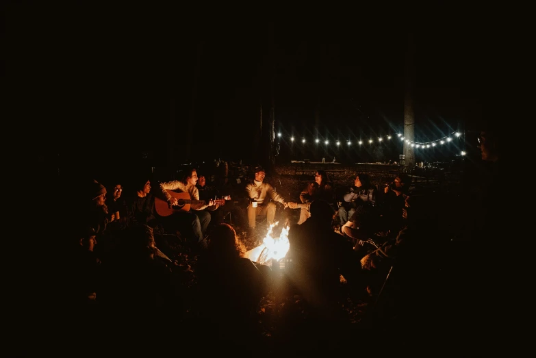 a group of people sitting around a fire pit at night