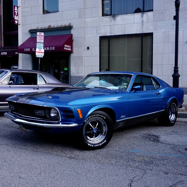 a blue mustang sits parked next to a silver car on a city street