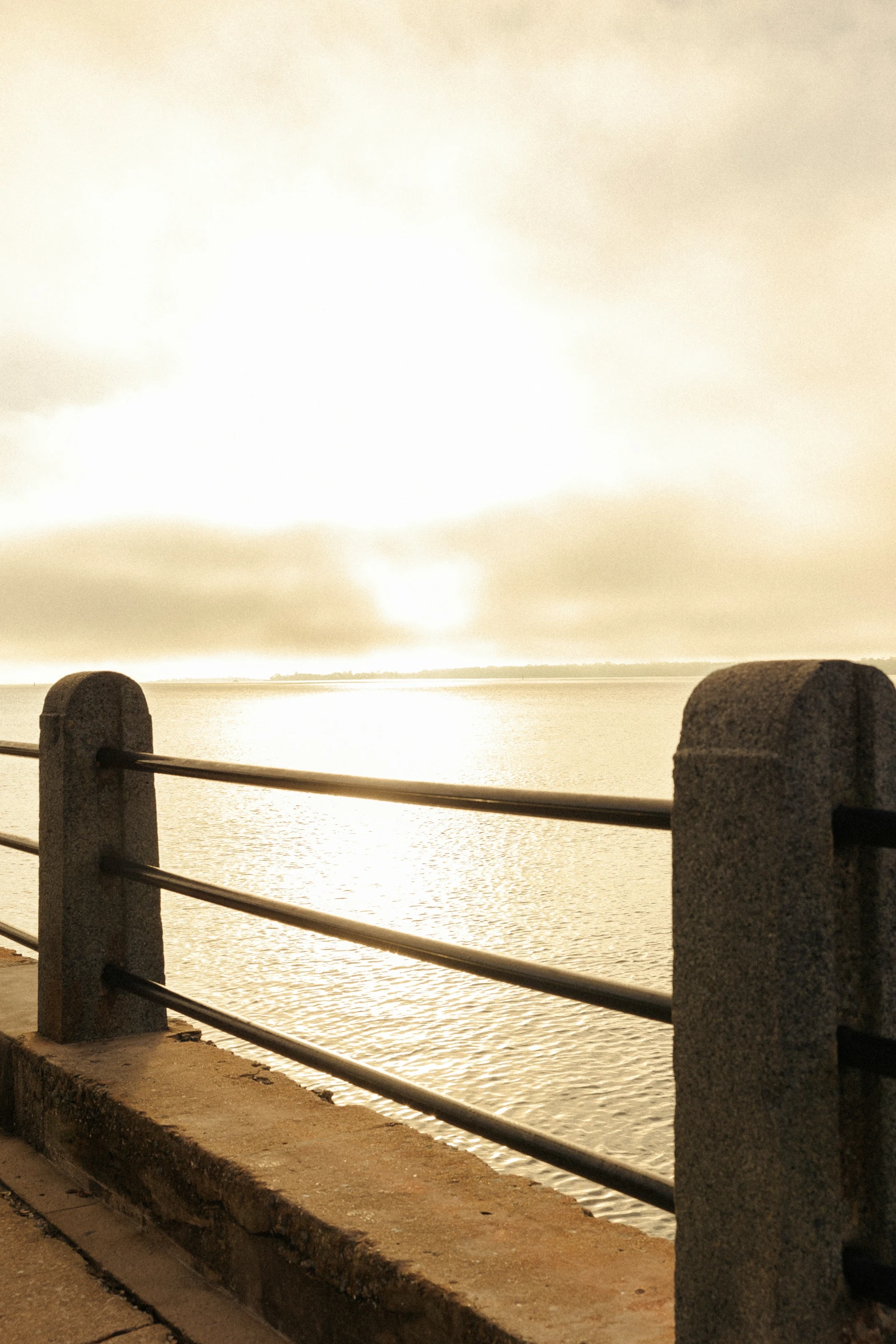 a man sitting on the railing of a long pier, looking at a large body of water