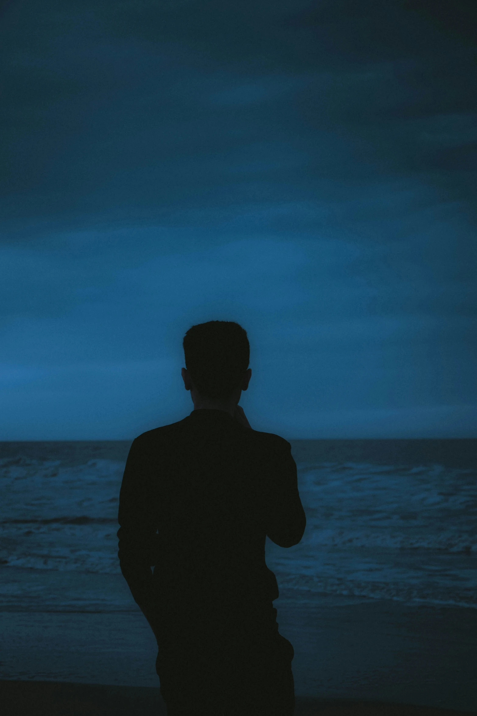 the silhouette of man standing on beach with ocean in the background