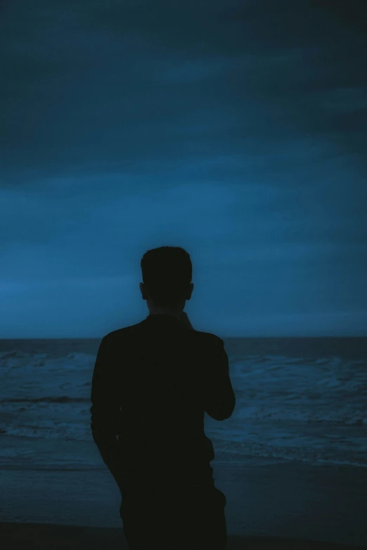 the silhouette of man standing on beach with ocean in the background