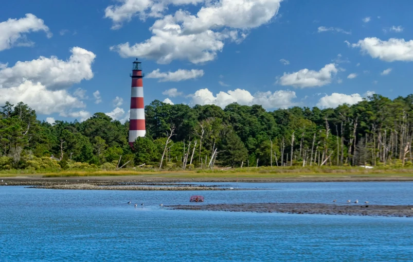 a boat traveling along the water in front of a lighthouse