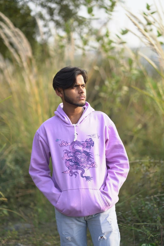 a man in a hoodie stands outside near tall grass