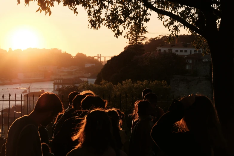 a crowd of people stand near a river as the sun sets