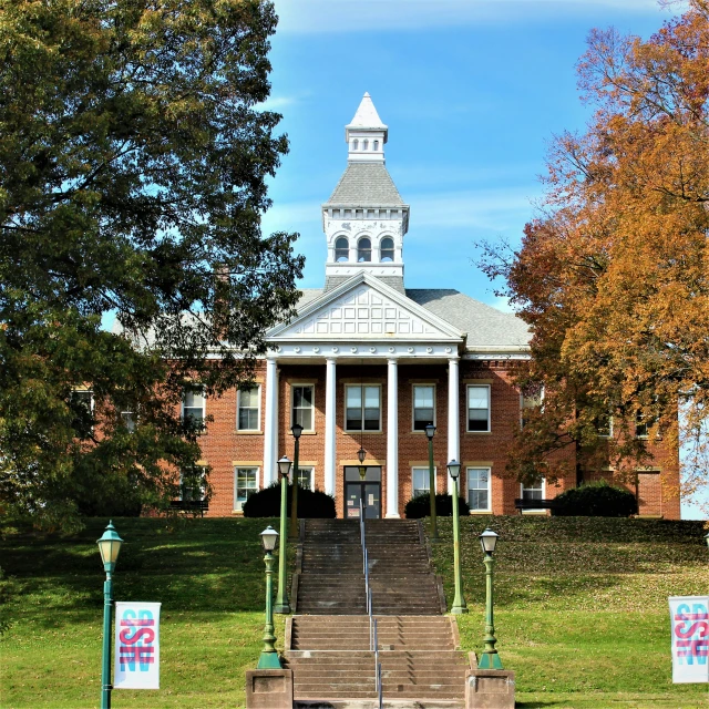 a brick building has a steeple, trees and bushes in front