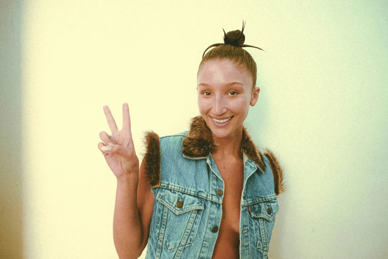 a girl wearing a denim vest shows her peace sign