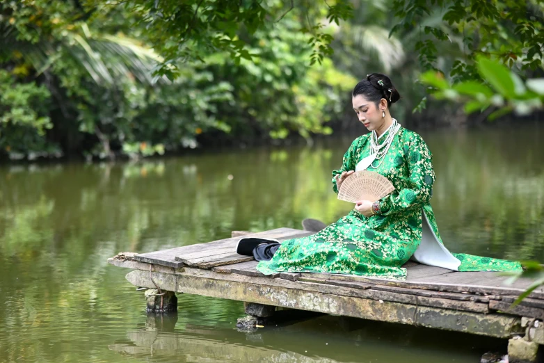 a woman in a green kimono sitting on a wooden pier