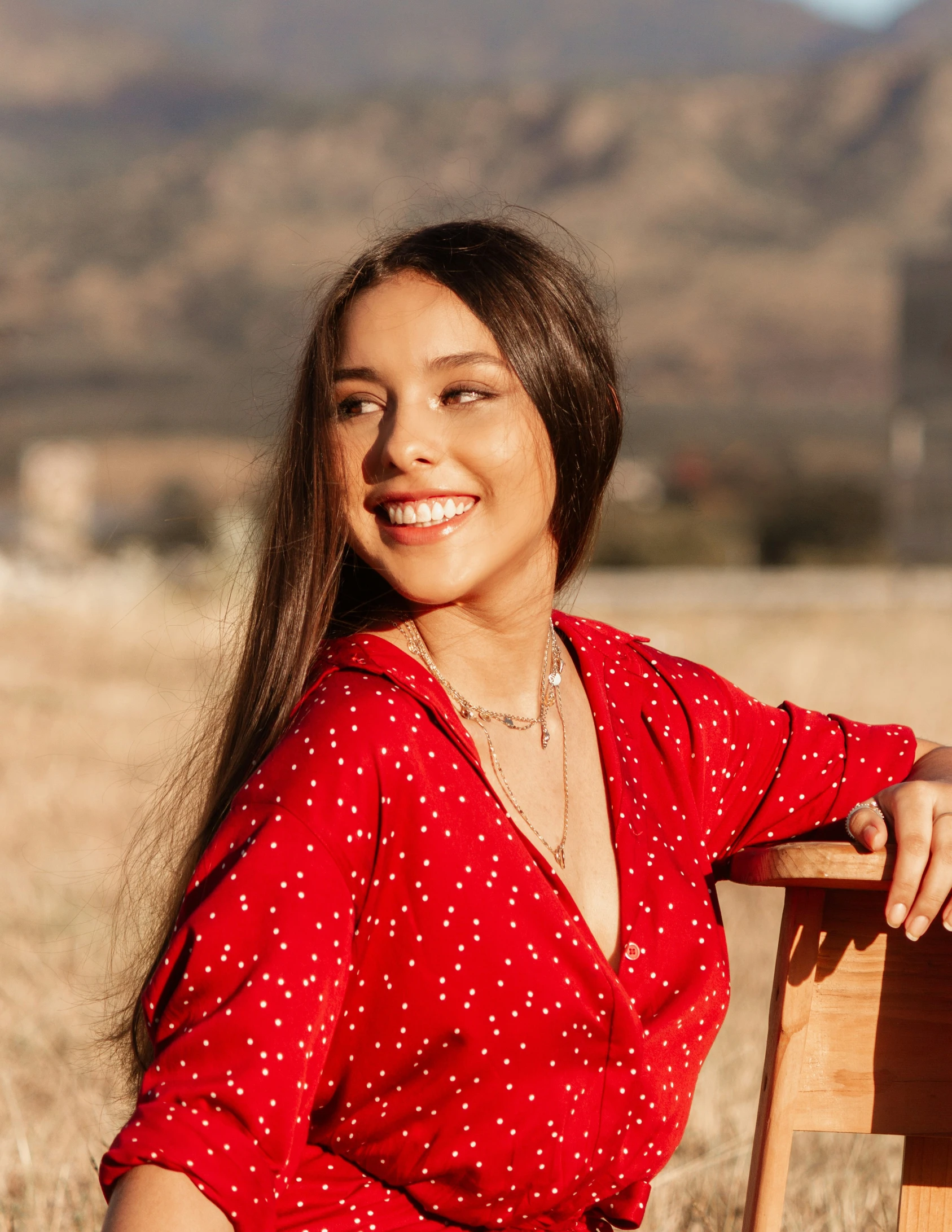 a young woman smiles while sitting on a wooden chair