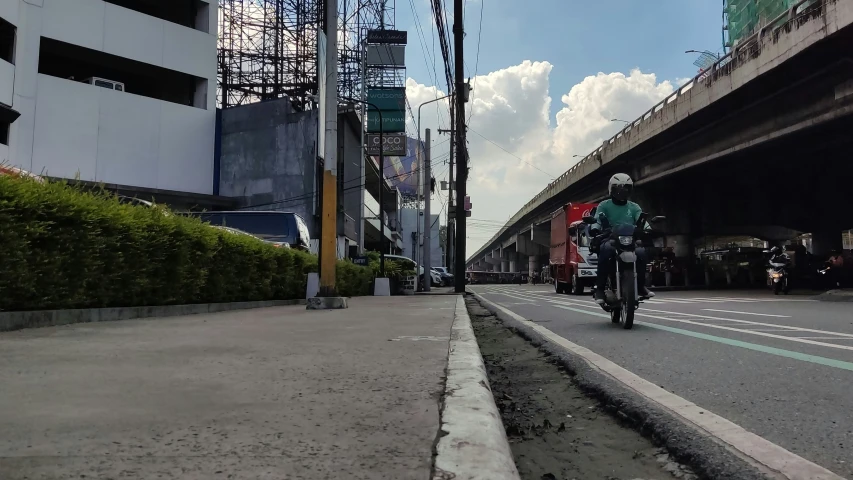 a man riding a motorcycle down a sidewalk next to a bridge