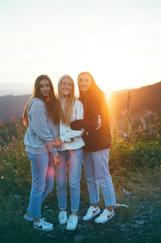 three girls standing together in a field at sunset