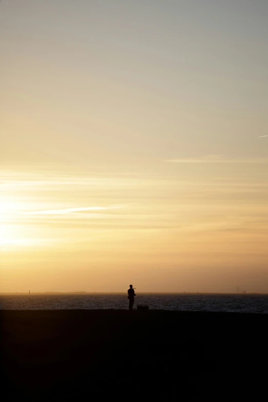 a person stands in the distance on the shore while the sun is setting