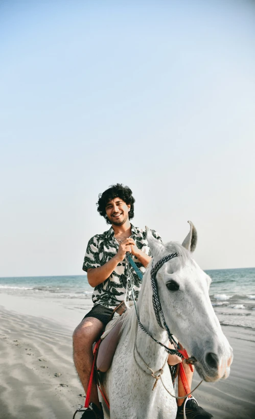 a man riding on the back of a white horse near the ocean