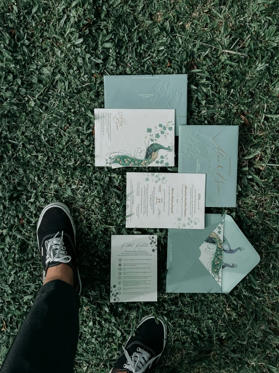 a person is standing on the grass with a sheet of paper, some papers and a pair of shoes