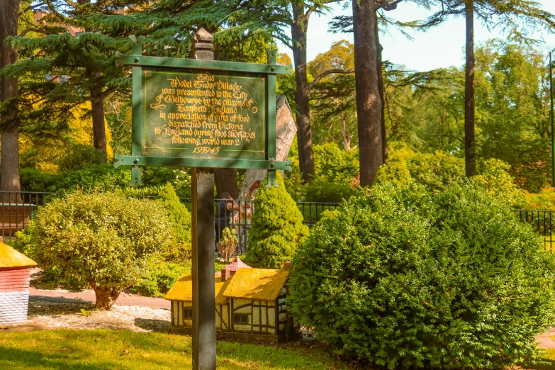 a green sign in a park with trees and bushes